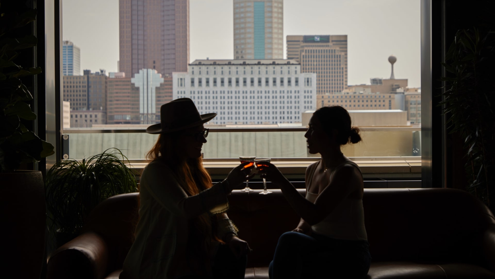 Two women clinking glasses in front of city scape window