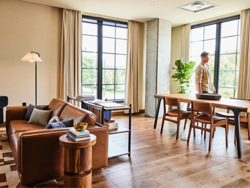 living room with couch, chairs, lighting and dining table with man walking by