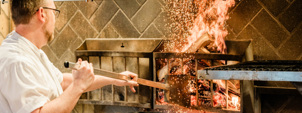 chef fanning a wood fire grill in a kitchen