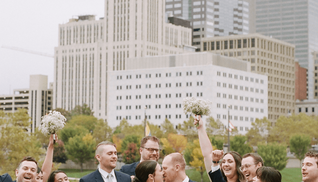 Bride and groom kissing with wedding party behind them