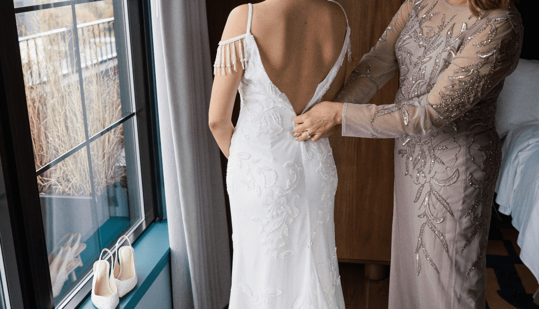 Woman in wedding dress with an older woman helping zip up the back