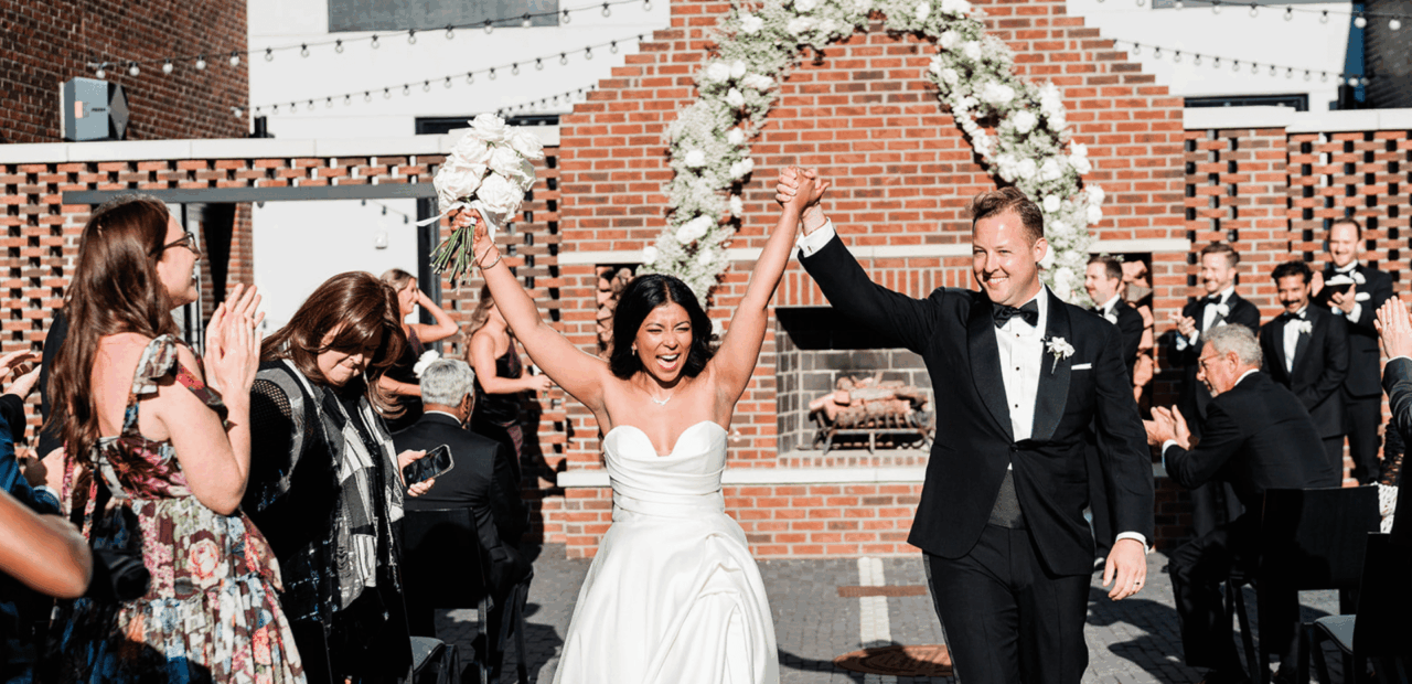 Man and woman walking down aisle holding hands up after getting married